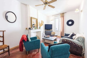 Ein Wohnzimmer mit türkis-blauen Sesseln, einem Fernseher und einem Deckenventilator.