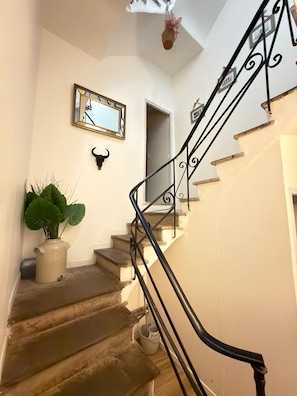 Eine Treppe mit schwarzer Metallreling, einem Topfpflanzen, einem gerahmten Spiegel und einer Wandleuchte.