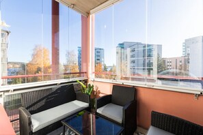 A balcony with wicker furniture, a glass table, and a view of buildings and trees. - Cozy Two-Bedroom Apartment - Private Sauna & Balcony (Jyväskylä)