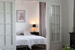 A bedroom with a bed, a nightstand, a lamp, a framed picture, and a door. - Cozy Two-Bedroom Apartment - Private Sauna & Balcony (Jyväskylä)