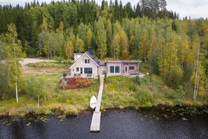 Una casa con un muelle que se adentra en un lago, rodeada de un bosque denso.