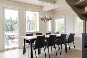 A dining area with a wooden table and black chairs, large windows, and a chandelier.