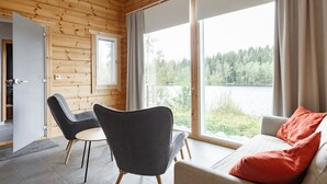 A cabin with a wooden interior, a sofa with red cushions, and a view of a lake. - Lakefront Holiday Villa - Traditional Finnish sauna & outdoor jacuzzi (Uurainen)