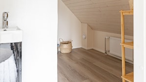 A room with a sloped ceiling, a white wall, a wooden floor, a white sink, a woven basket, and a wooden shelf. - Lakefront Holiday Villa - Traditional Finnish sauna & outdoor jacuzzi (Uurainen)