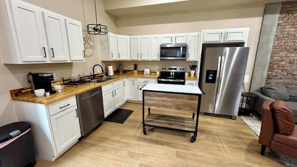 A modern kitchen with white cabinets, stainless steel appliances, a coffee maker, and a cart.
