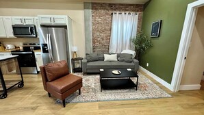 A compact living space with a kitchenette, a sofa, a coffee table, and a brick accent wall.