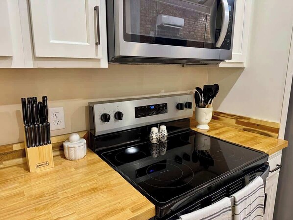 A kitchen with a black stove, white cabinets, a microwave above, and a wooden countertop. - Modern Boho Getaway 1BR Apartment By KeenStays (Cape Girardeau)