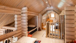 A log cabin interior with a loft bedroom, wooden beams, and a small staircase.