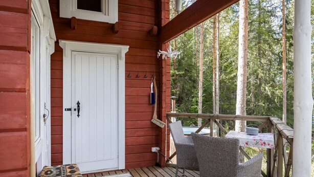 A wooden deck with wicker chairs, a white door, and a small table with a floral tablecloth.