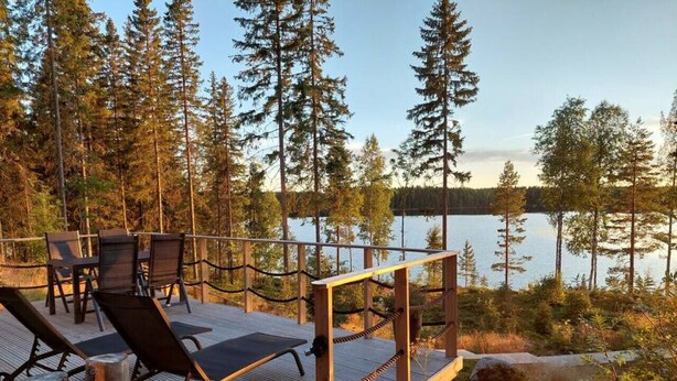 A wooden deck with chairs and a table overlooking a lake, surrounded by trees.