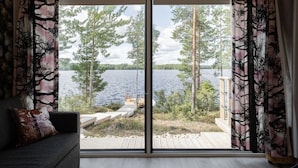Una habitación con un gran ventanal corredero que da a una terraza de madera con vistas a un lago.