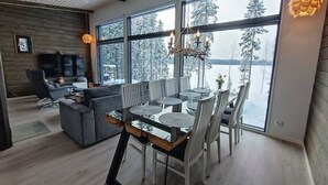 Un comedor moderno con una mesa de vidrio, sillas blancas y vistas a un paisaje nevado a través de amplios ventanales.