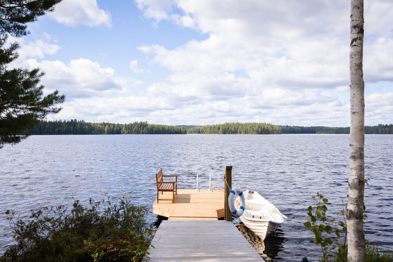A wooden dock extending into a calm lake, a bench, and a small boat with a life ring.