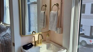 A bathroom with a white sink, gold fixtures, a mirror, and a window with a view of a building.