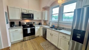 A compact kitchen with white cabinets, a stainless steel refrigerator, a microwave, an oven, a dishwasher, and a granite countertop.