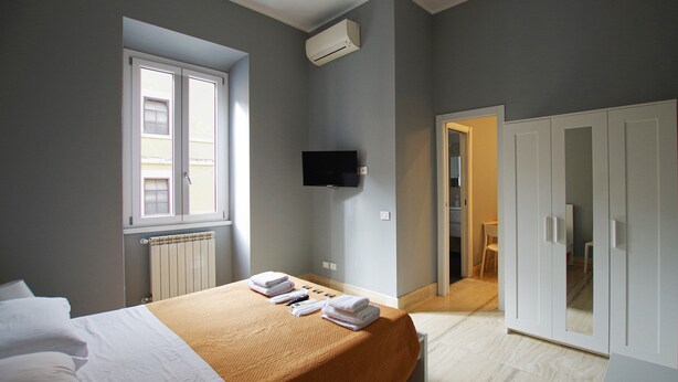 A hotel room with a bed, a TV, a radiator, and a wardrobe. - Apartment with 2 double bedrooms (Roma)