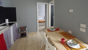 A compact kitchen with a dining area, a small storage unit, and a visible bedroom through an open door. - Apartment with 2 double bedrooms (Roma)