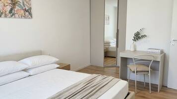Ein Schlafzimmer mit Bett, Nachttisch, Schreibtisch mit Stuhl, Spiegel und einer Pflanze.