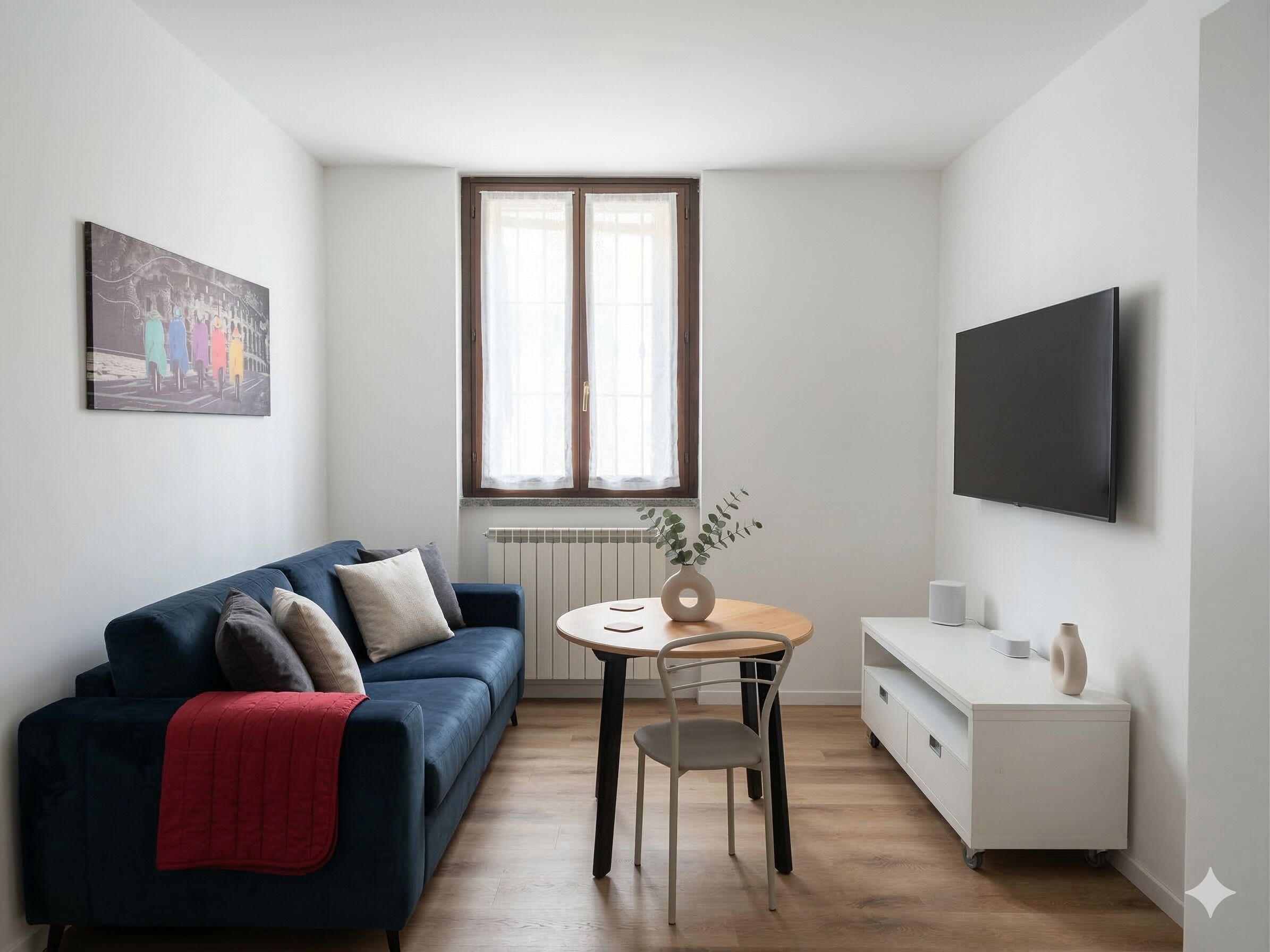 Ein modernes Wohnzimmer mit einem blauen Sofa, einem kleinen runden Tisch, einer weißen Kommode und einem an der Wand montierten Fernseher.