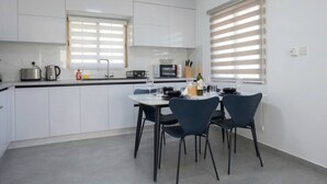 Une cuisine moderne avec des meubles blancs, une table à manger avec des chaises et une fenêtre avec des stores.