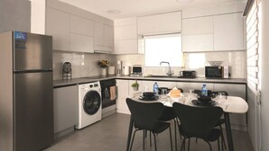 Une cuisine moderne équipée d’un réfrigérateur en acier inoxydable, d’un lave-linge, d’un four à micro-ondes et d’un coin repas avec des chaises noires.