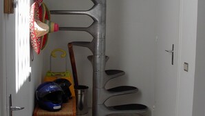 Une pièce d’angle avec un escalier en colimaçon, un panier en osier et un casque posé sur le sol.