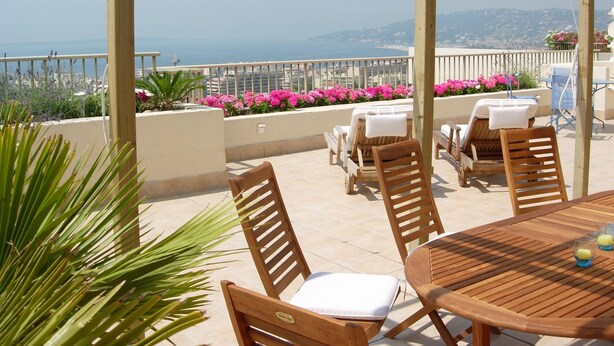 Une table en bois avec des chaises, une vue sur la mer et des fleurs roses.