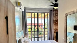 Une chambre à coucher avec un lit, un ventilateur de plafond, une fenêtre avec des rideaux et une vue sur l’extérieur.
