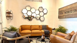 Un salon comprenant un canapé, un fauteuil et une table basse, ainsi qu’un élément décoratif mural hexagonal et une enseigne portant l’inscription « CASA MORELOS ».