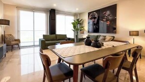 Een moderne woonkamer met een eethoek, een groene bank, een groot schilderij en een raam van de vloer tot aan het plafond.
