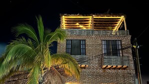 A two-story building with a brick facade, a balcony with string lights, and a palm tree in the foreground. - TS4 King in Todos Santos (Todos Santos)