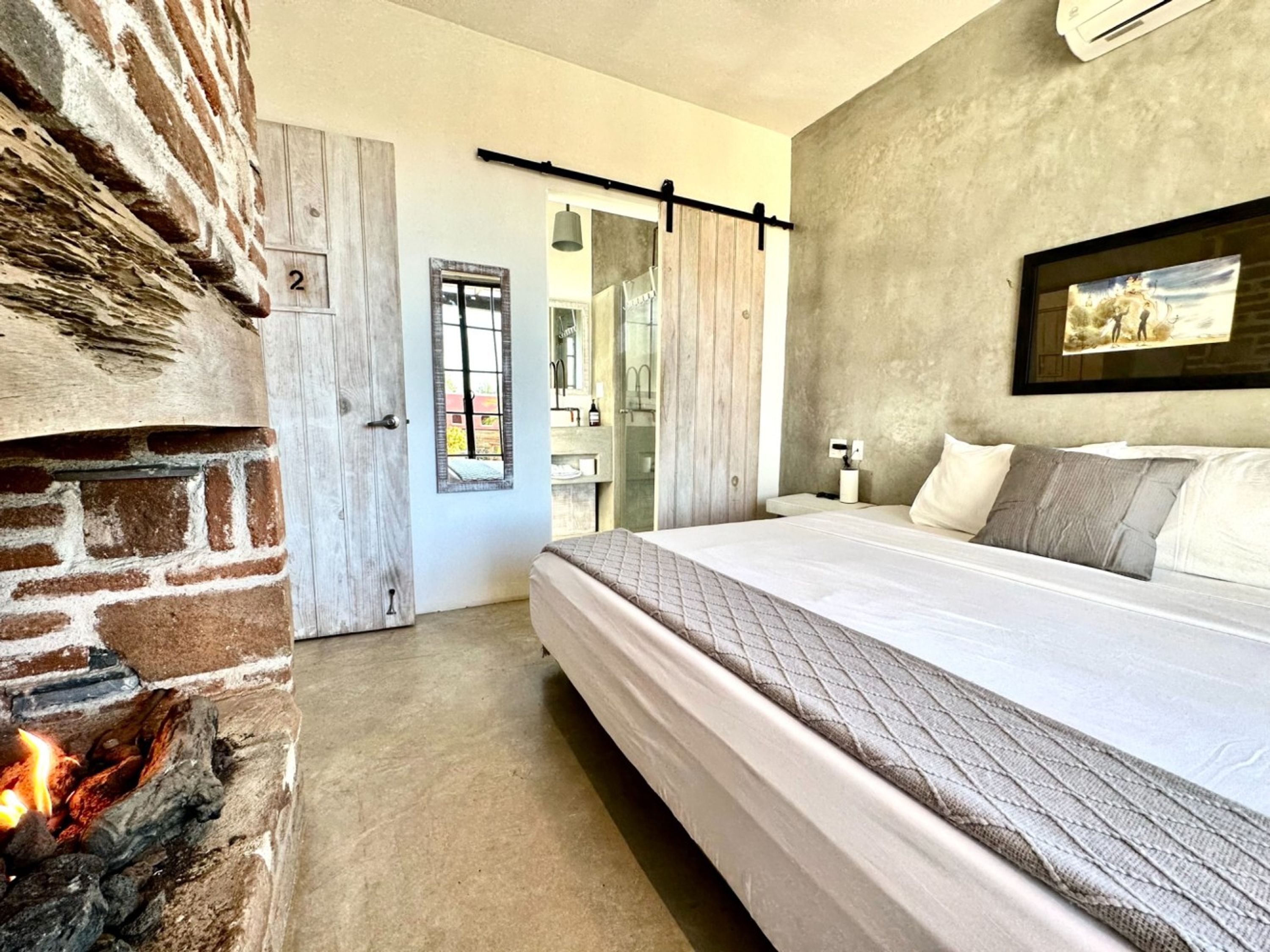 Una camera da letto con camino in mattoni, un letto con copripiumino trapuntato, un quadro appeso e una porta con un numero.