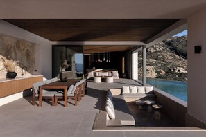 A modern interior with a dining area, seating, and a view of the sea. - Crimson View Villa by Hide Out (Ios)