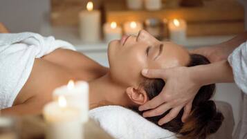 A person receiving a head massage in a spa setting with candles and a wooden shelf in the background.
