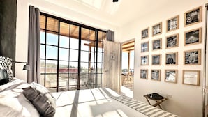 Ein Schlafzimmer mit großem Fenster, einem Bett mit gestreifter Bettwäsche, einem Nachttisch und einer Wand mit gerahmten Bildern.