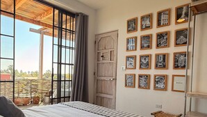 Een slaapkamer met een groot bed, een plafondventilator, een houten deur en een muur met ingelijste foto's.