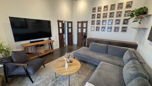 Een woonkamer met een grote flatscreen televisie, een grijze bank, een houten salontafel en een grijze fauteuil.