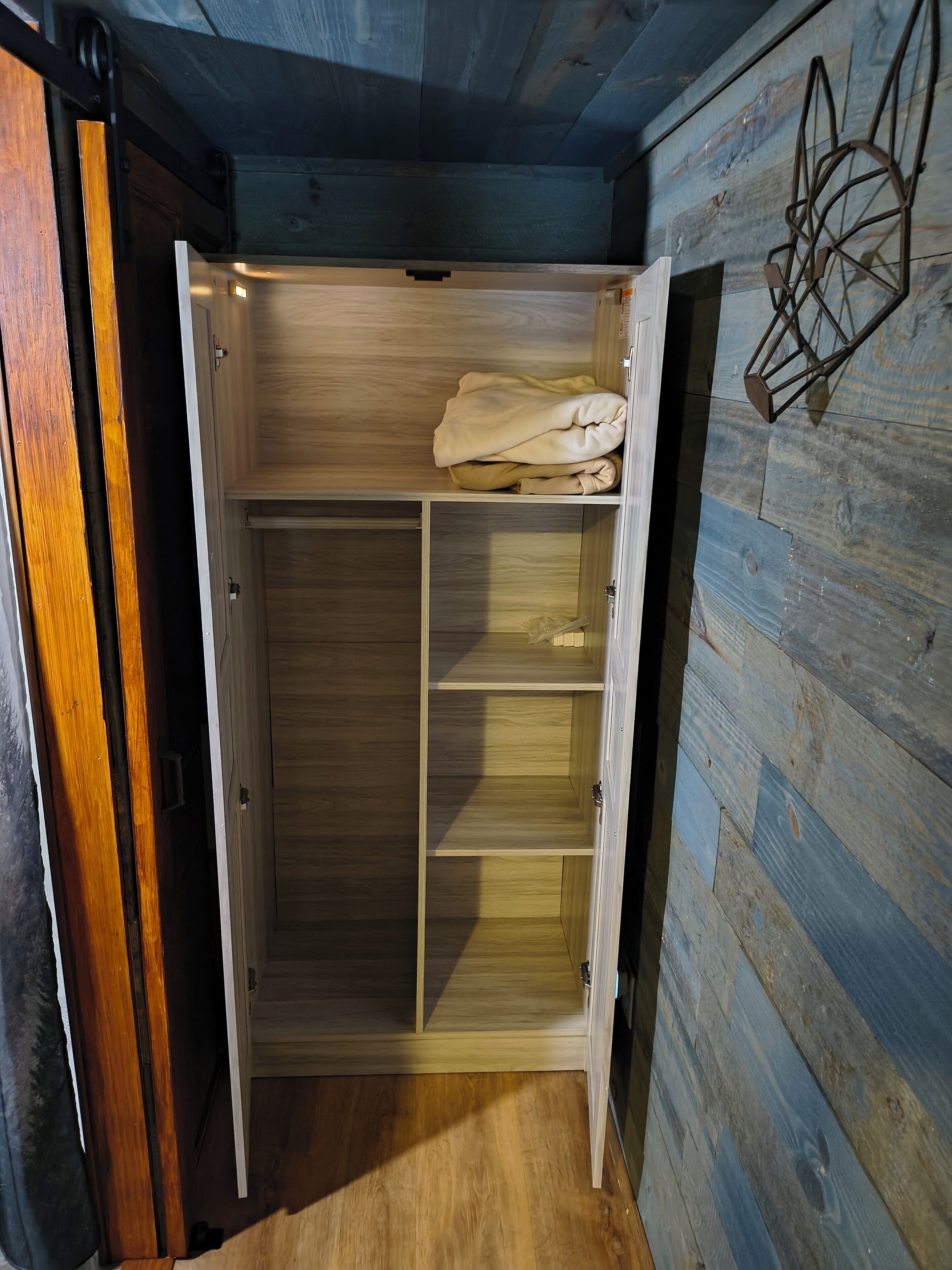 A wooden wardrobe with multiple shelves and a hanging rod, partially open.