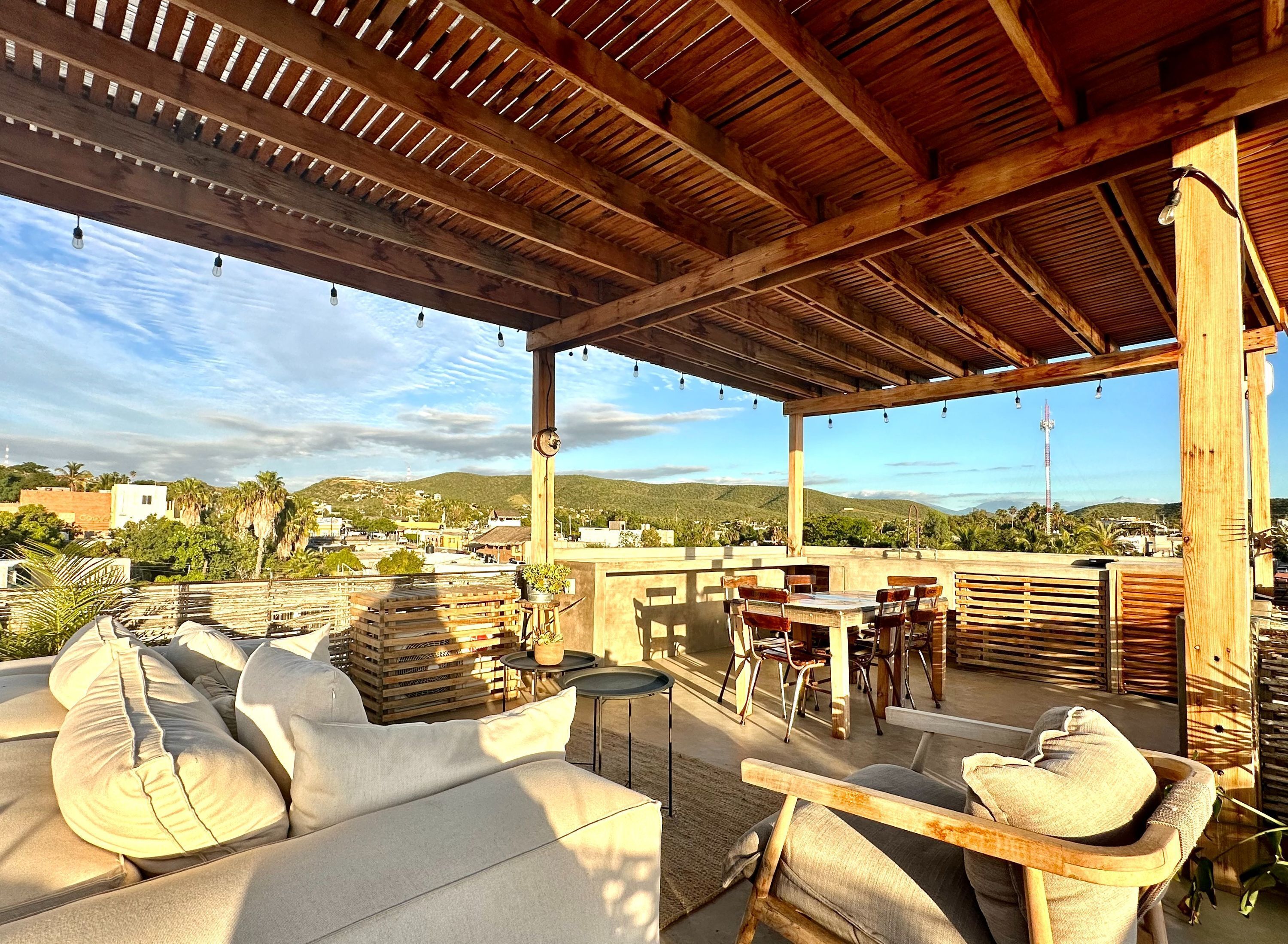 Eine Terrass mit Holzmöbeln, einer Pergola und Blick auf eine Stadt und Hügel.
