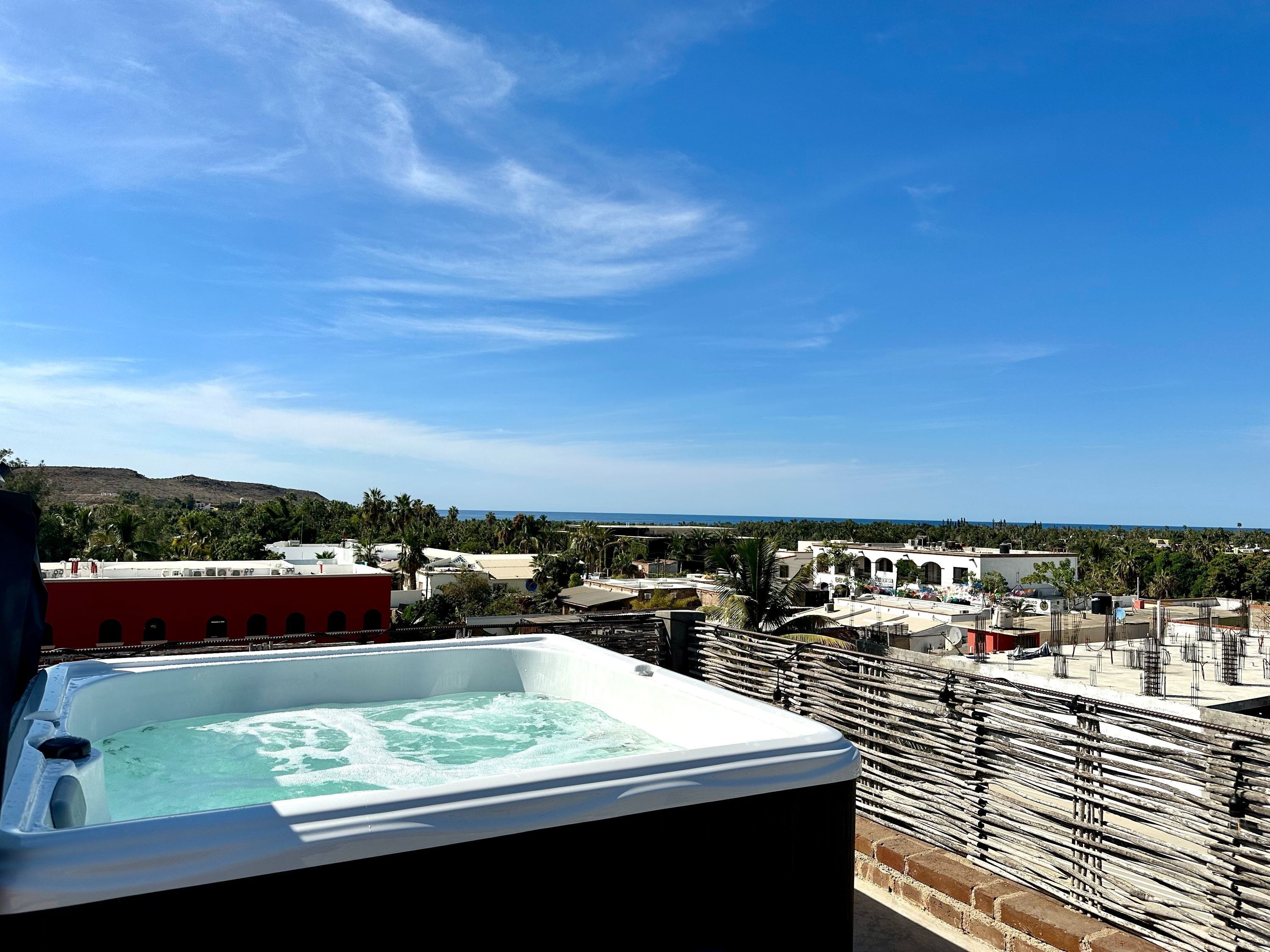 A rooftop with a hot tub, a view of the city, and a distant coastline.
