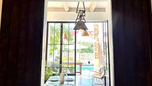 A room with a large wooden table, a hanging light fixture, and a view of an outdoor area with a pool and patio furniture. - TS5 King in Todos Santos (Todos Santos)