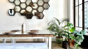 A dining area with a hexagonal mirror wall, a wooden table with plates, a vase, and potted plants. - TS5 King in Todos Santos (Todos Santos)