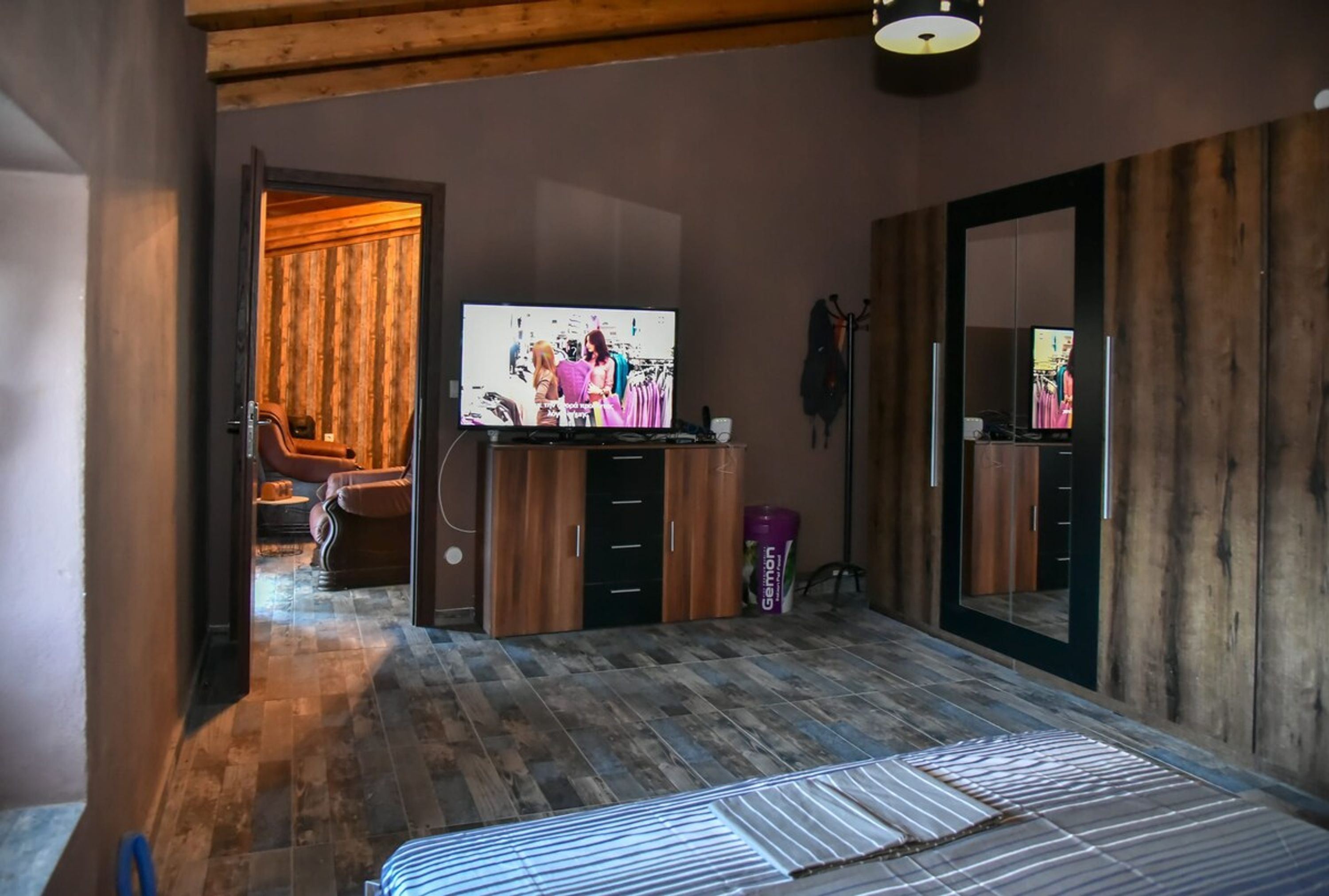 Un dormitorio con techo de madera, una cama con colcha a rayas, un televisor sobre un mueble de madera y un armario con espejo.