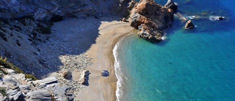 Un paysage côtier caractérisé par un terrain rocheux, des eaux d’un bleu limpide et une plage de sable.