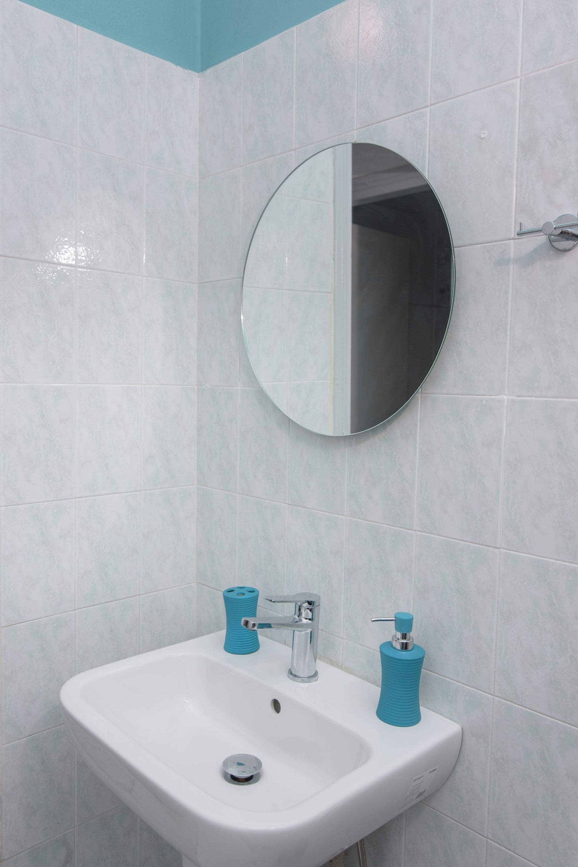 Een badkamer met een wit wastafel, een ronde spiegel en twee blauwe zeepdispensers.