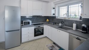 Uma cozinha moderna com armários brancos, geladeira de aço inoxidável, micro-ondas, forno, lava-louças e uma janela com vista.