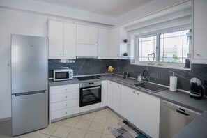 A modern kitchen with white cabinets, a stainless steel refrigerator, a microwave, an oven, a dishwasher, and a window with a view. - Angel Apartment at Amoudara (Malevizi)