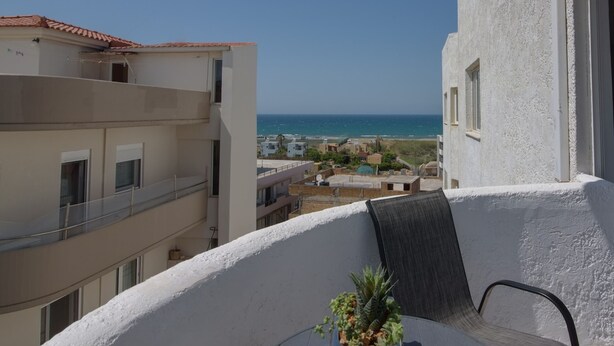 Varanda com vista para o mar, uma cadeira e uma pequena mesa com uma planta.