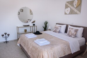 A neatly made bed with a large round mirror, a bedside table with a decorative item, and a wall art piece. - Angel Apartment at Amoudara (Malevizi)