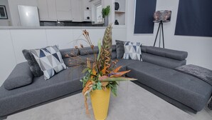 Uma sala de estar moderna com um sofá modular cinza, um vaso amarelo com plantas secas e um abajur de chão.